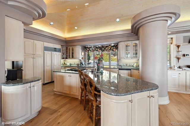 kitchen featuring a kitchen island, light hardwood / wood-style floors, dark stone counters, and decorative columns