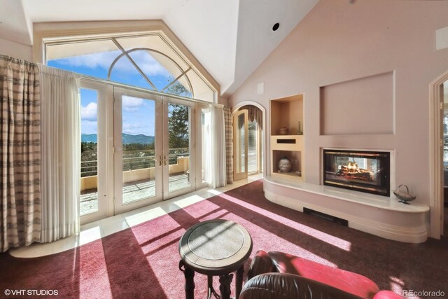 carpeted living room with a multi sided fireplace, a mountain view, french doors, and vaulted ceiling