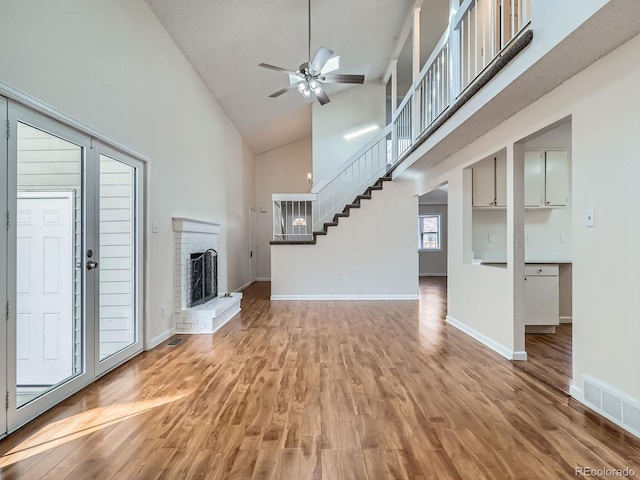 unfurnished living room featuring hardwood / wood-style flooring, ceiling fan, a brick fireplace, and a high ceiling