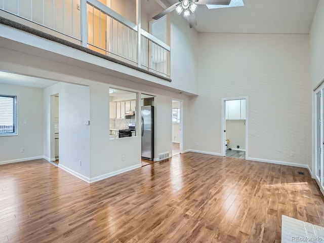 unfurnished living room with ceiling fan, wood-type flooring, and a high ceiling