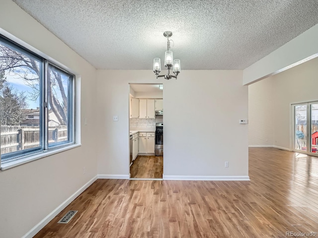 unfurnished dining area with a textured ceiling, a chandelier, and light wood-type flooring