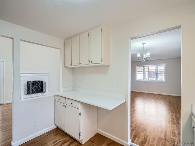 kitchen featuring a fireplace, white cabinetry, wood-type flooring, a chandelier, and hanging light fixtures