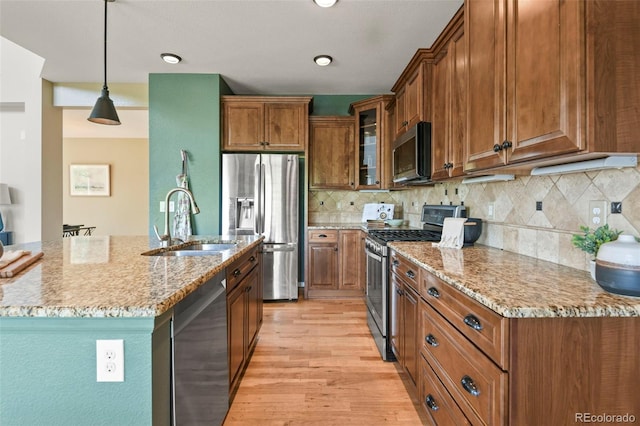 2815 Dreamcatcher Loop, Castle Rock, CO 80109 - kitchen with stainless steel appliances, brown cabinetry, light wood finished floors, light stone countertops, and glass insert cabinets