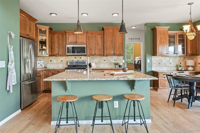2815 Dreamcatcher Loop, Castle Rock, CO 80109 - kitchen featuring stainless steel appliances, brown cabinetry, tasteful backsplash, washer / clothes dryer, and light wood-type flooring