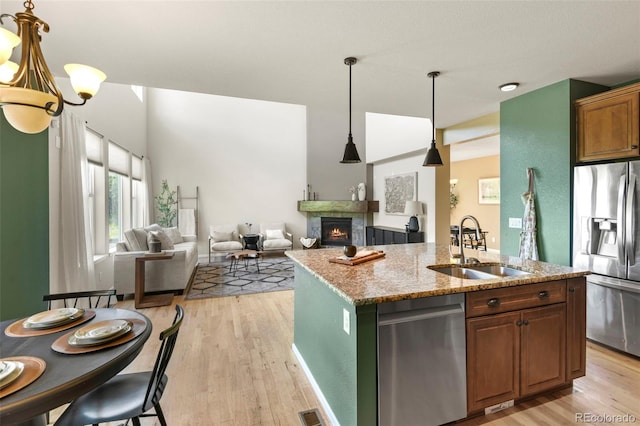 2815 Dreamcatcher Loop, Castle Rock, CO 80109 - kitchen with stainless steel appliances, light wood-type flooring, a center island with sink, a warm lit fireplace, and light stone counters