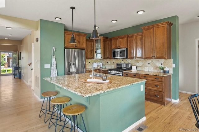 2815 Dreamcatcher Loop, Castle Rock, CO 80109 - kitchen featuring appliances with stainless steel finishes, light wood-style floors, light stone counters, tasteful backsplash, and brown cabinetry