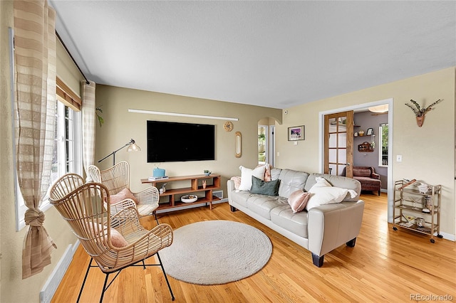 living area featuring light wood-type flooring, arched walkways, and baseboards