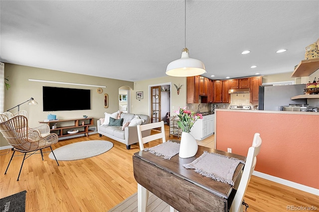 dining area featuring arched walkways, baseboards, recessed lighting, and light wood-style flooring