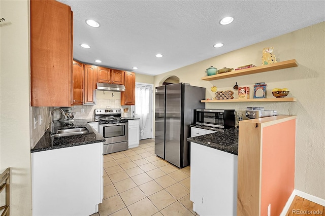 kitchen with a sink, dark stone countertops, stainless steel appliances, tasteful backsplash, and under cabinet range hood