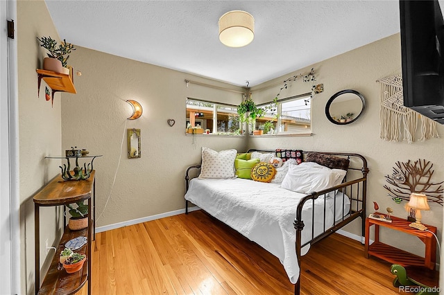 bedroom featuring baseboards, a textured ceiling, a textured wall, and wood finished floors