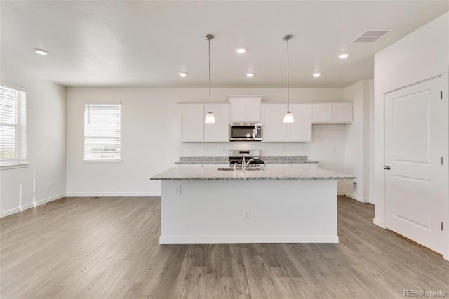 kitchen with appliances with stainless steel finishes, a sink, white cabinets, light stone counters, and a center island with sink