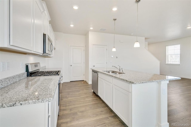 kitchen with appliances with stainless steel finishes, a sink, white cabinetry, light wood-type flooring, and a kitchen island with sink