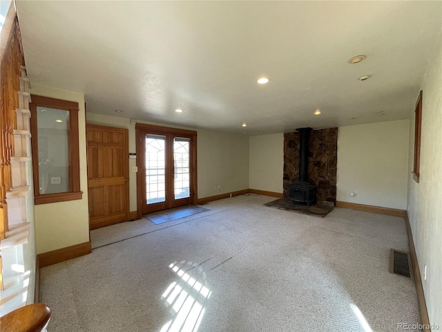 unfurnished living room with french doors, light colored carpet, and a wood stove