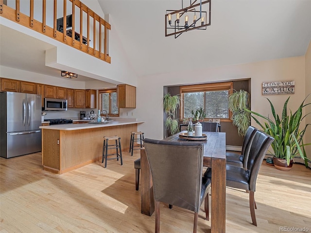 dining area featuring a baseboard heating unit, a notable chandelier, a towering ceiling, and light wood finished floors