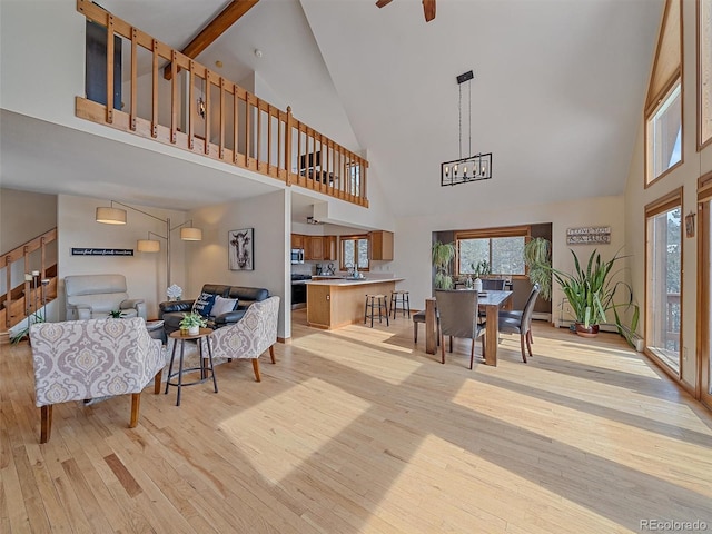 living room featuring a high ceiling, light wood-style floors, a healthy amount of sunlight, and ceiling fan