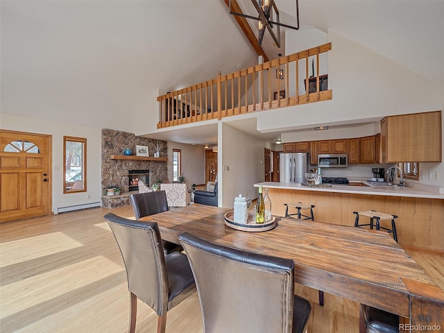 dining area with baseboard heating, light wood-style flooring, a fireplace, and high vaulted ceiling