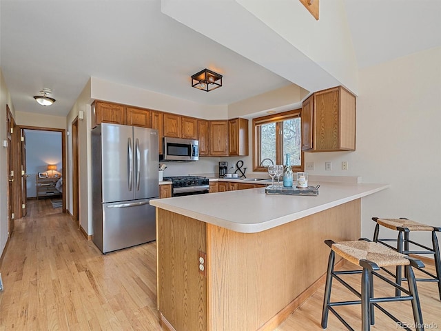 kitchen featuring light countertops, appliances with stainless steel finishes, a peninsula, light wood-style floors, and a sink