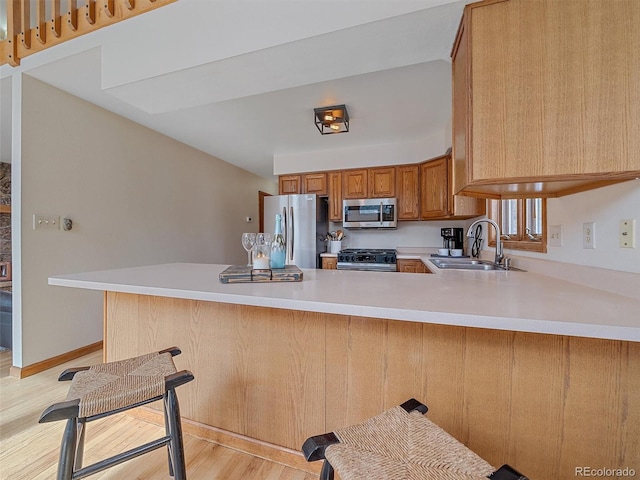 kitchen featuring brown cabinetry, a peninsula, a sink, light countertops, and appliances with stainless steel finishes