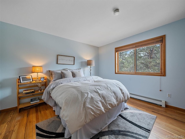 bedroom with a baseboard heating unit, wood finished floors, and baseboards