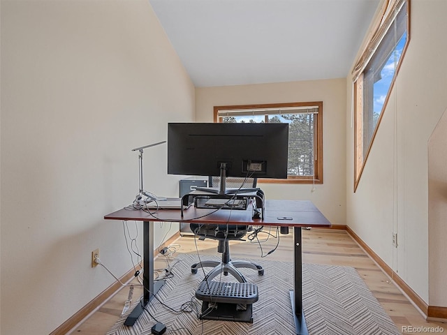 office space featuring light wood finished floors, baseboards, and vaulted ceiling