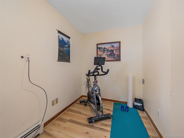 exercise room featuring baseboard heating, light wood-type flooring, and baseboards