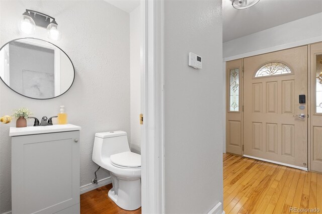 half bath featuring vanity, toilet, baseboards, and hardwood / wood-style floors