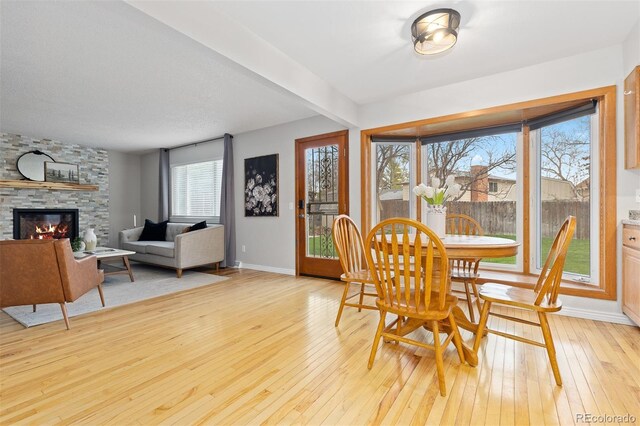 dining room featuring light wood-type flooring, baseboards, and a stone fireplace