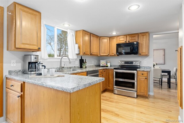 kitchen featuring a peninsula, light countertops, a sink, light wood finished floors, and stainless steel appliances