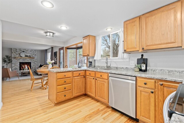 kitchen with a sink, dishwasher, a stone fireplace, a peninsula, and light wood-type flooring