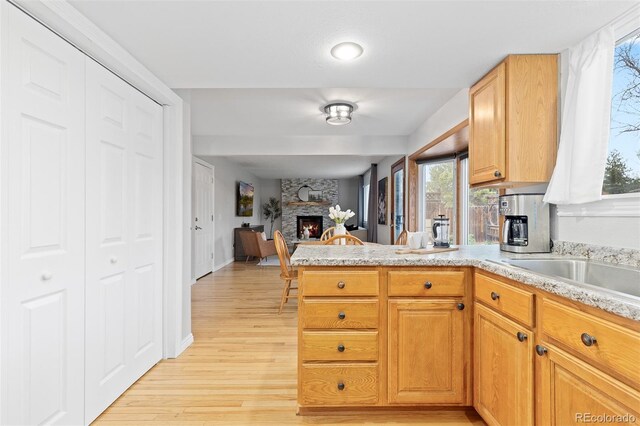 kitchen with a peninsula, light countertops, a fireplace, and light wood finished floors