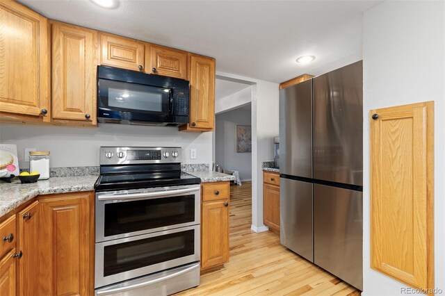 kitchen with light stone countertops, recessed lighting, brown cabinets, light wood finished floors, and appliances with stainless steel finishes