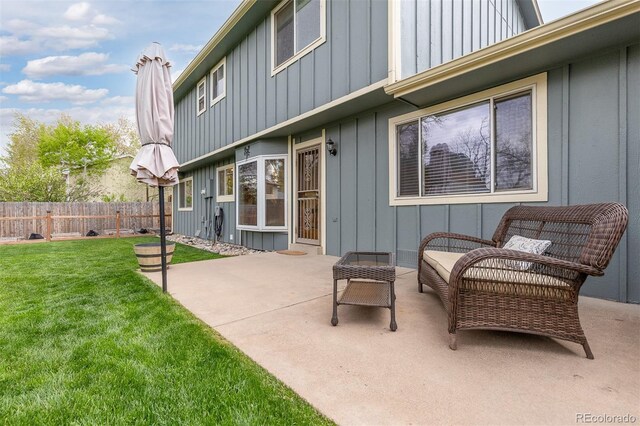 rear view of property with a patio, board and batten siding, fence, and a lawn