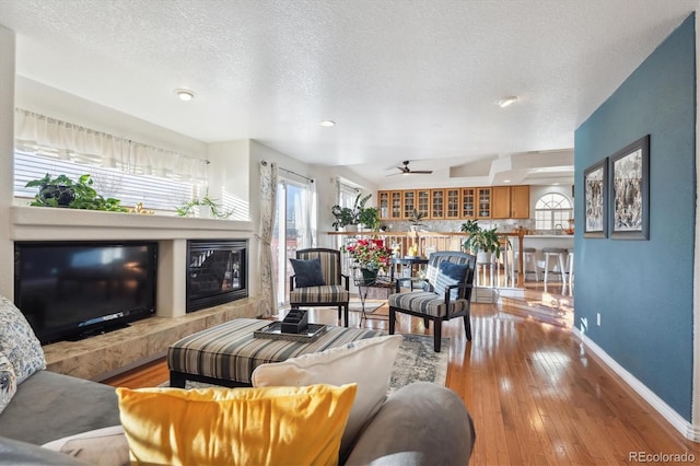 living room featuring a tiled fireplace, ceiling fan, light hardwood / wood-style flooring, and a textured ceiling