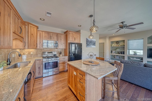 kitchen featuring visible vents, light wood-type flooring, a sink, black appliances, and open floor plan