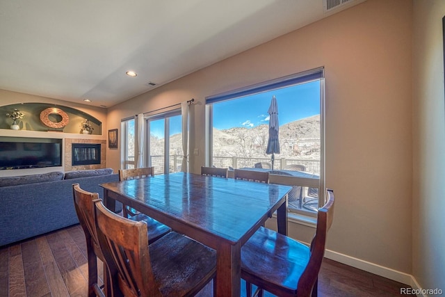 dining space with built in shelves, baseboards, recessed lighting, dark wood-type flooring, and a tiled fireplace