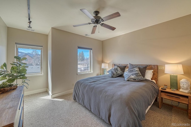 bedroom with visible vents, baseboards, light colored carpet, rail lighting, and a ceiling fan