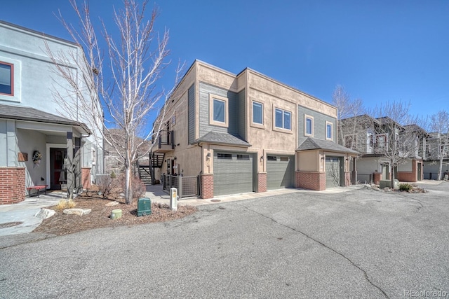 multi unit property featuring brick siding, stairway, a residential view, driveway, and an attached garage