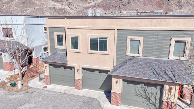 view of front facade featuring brick siding, aphalt driveway, roof with shingles, stucco siding, and a garage