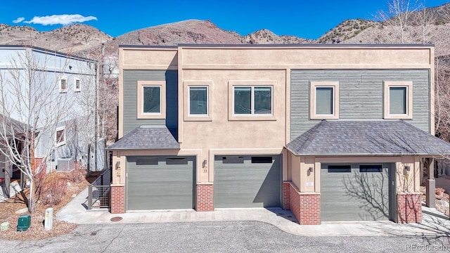 view of front of home featuring stucco siding, a mountain view, an attached garage, a shingled roof, and brick siding