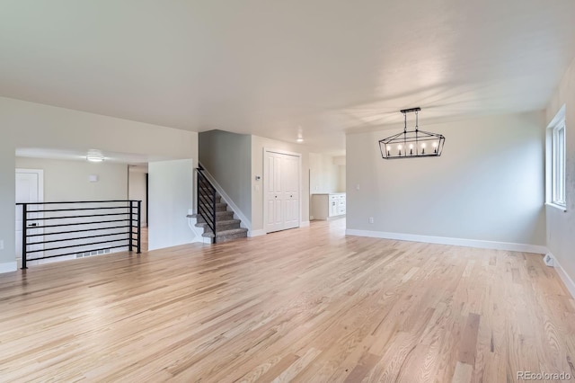 unfurnished living room with light wood-style floors, a notable chandelier, baseboards, and stairs