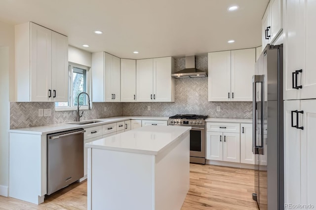 kitchen featuring wall chimney exhaust hood, appliances with stainless steel finishes, light wood-style floors, white cabinetry, and a sink