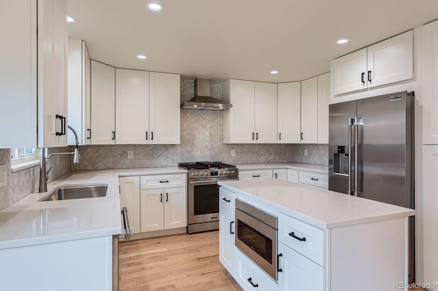 kitchen featuring stainless steel appliances, light countertops, a sink, wall chimney range hood, and light wood-type flooring