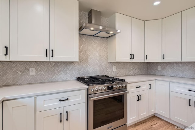 kitchen with white cabinetry, light countertops, wall chimney range hood, stainless steel gas range, and tasteful backsplash