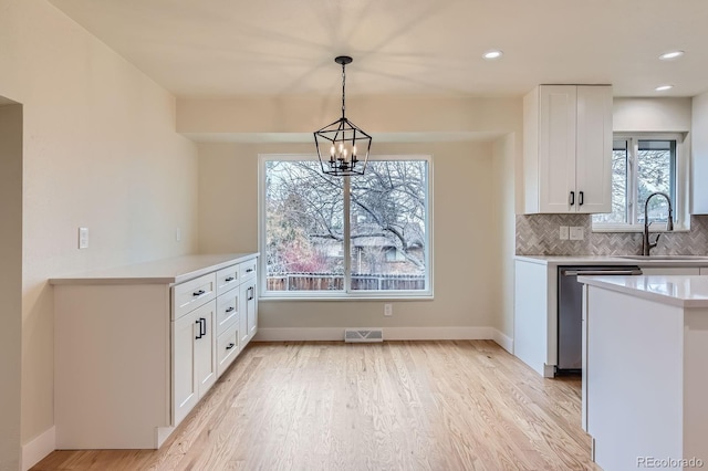 kitchen featuring a sink, white cabinetry, stainless steel dishwasher, decorative backsplash, and light wood finished floors