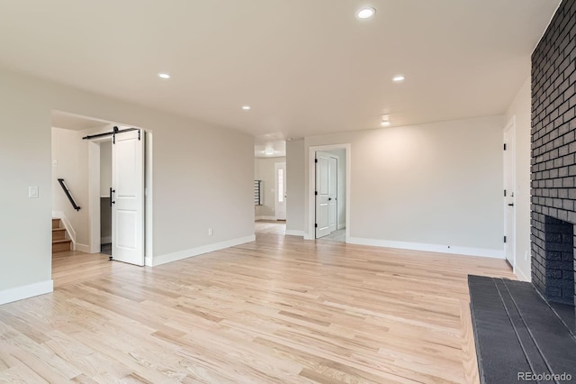 unfurnished living room with a barn door, recessed lighting, baseboards, light wood-style floors, and a brick fireplace