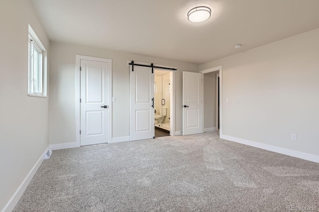 unfurnished bedroom with carpet floors, visible vents, ensuite bathroom, a barn door, and baseboards