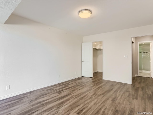 unfurnished bedroom featuring a spacious closet, a closet, and dark wood-type flooring