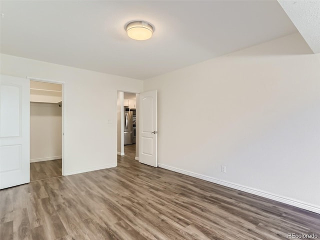 unfurnished bedroom featuring stainless steel refrigerator, a closet, dark hardwood / wood-style flooring, and a spacious closet