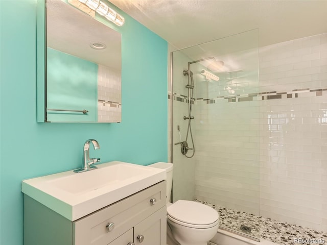 bathroom with a tile shower, vanity, and toilet