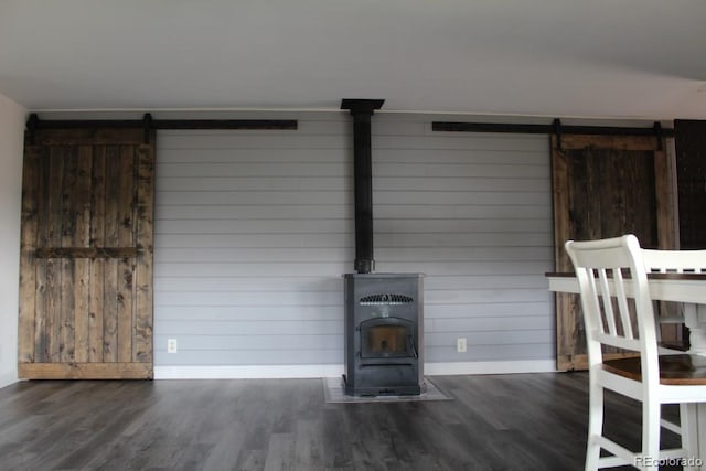 unfurnished living room featuring dark wood-type flooring, a barn door, and a wood stove